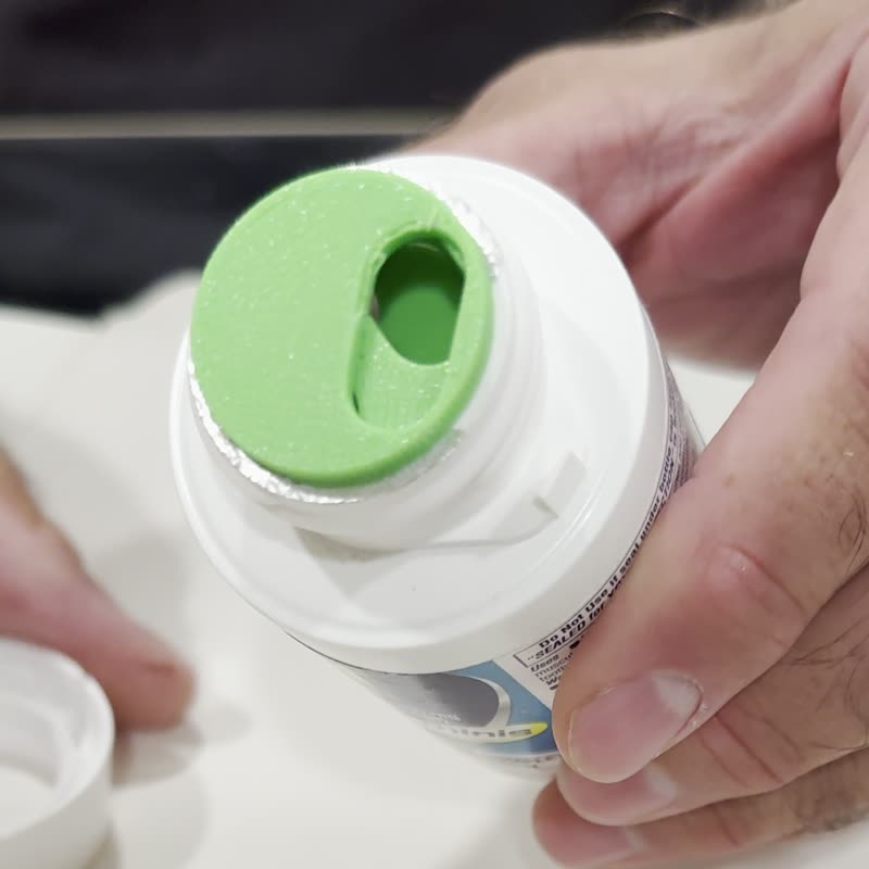A PillTwist insert, a green disc with a single slot, fitted in the neck of a pill bottle.